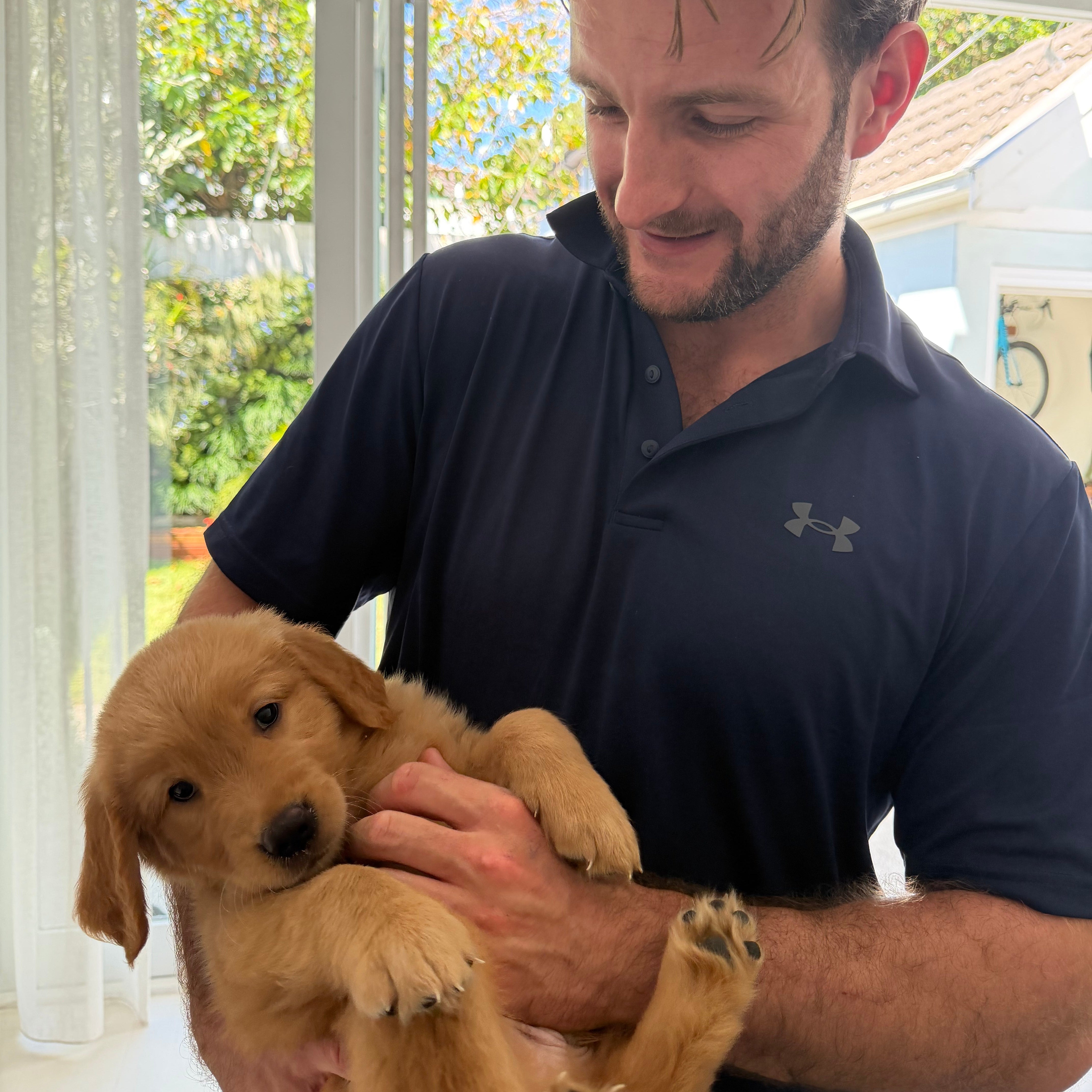 Man holding a puppy indoors with a window in the background