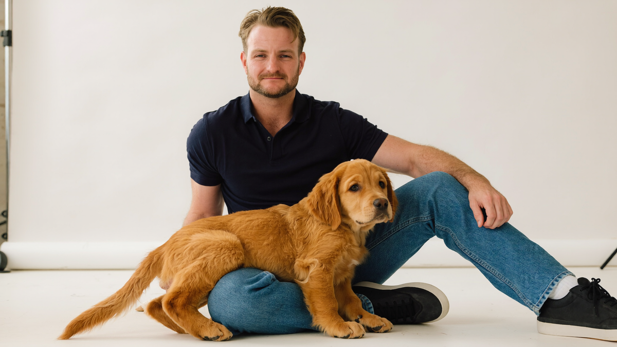 Sydney dog trainer Luke Buchanan sitting on a studio floor with a Goldador puppy in his lap