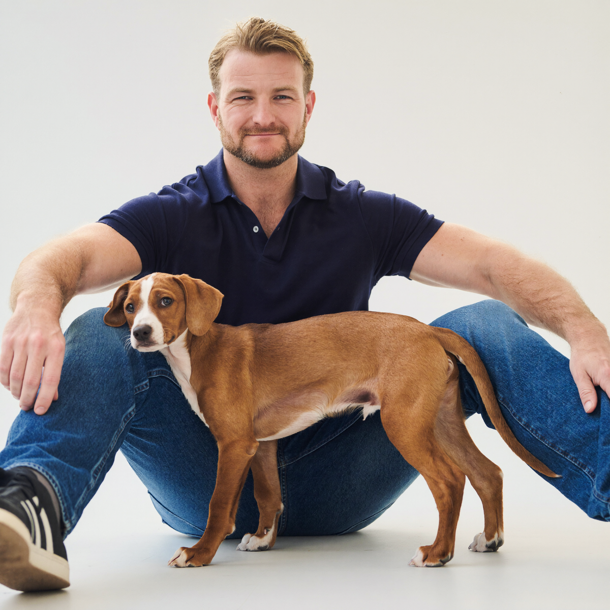Sydney dog trainer Luke Buchanan sitting on a studio floor with a Greyhound puppy in his lap